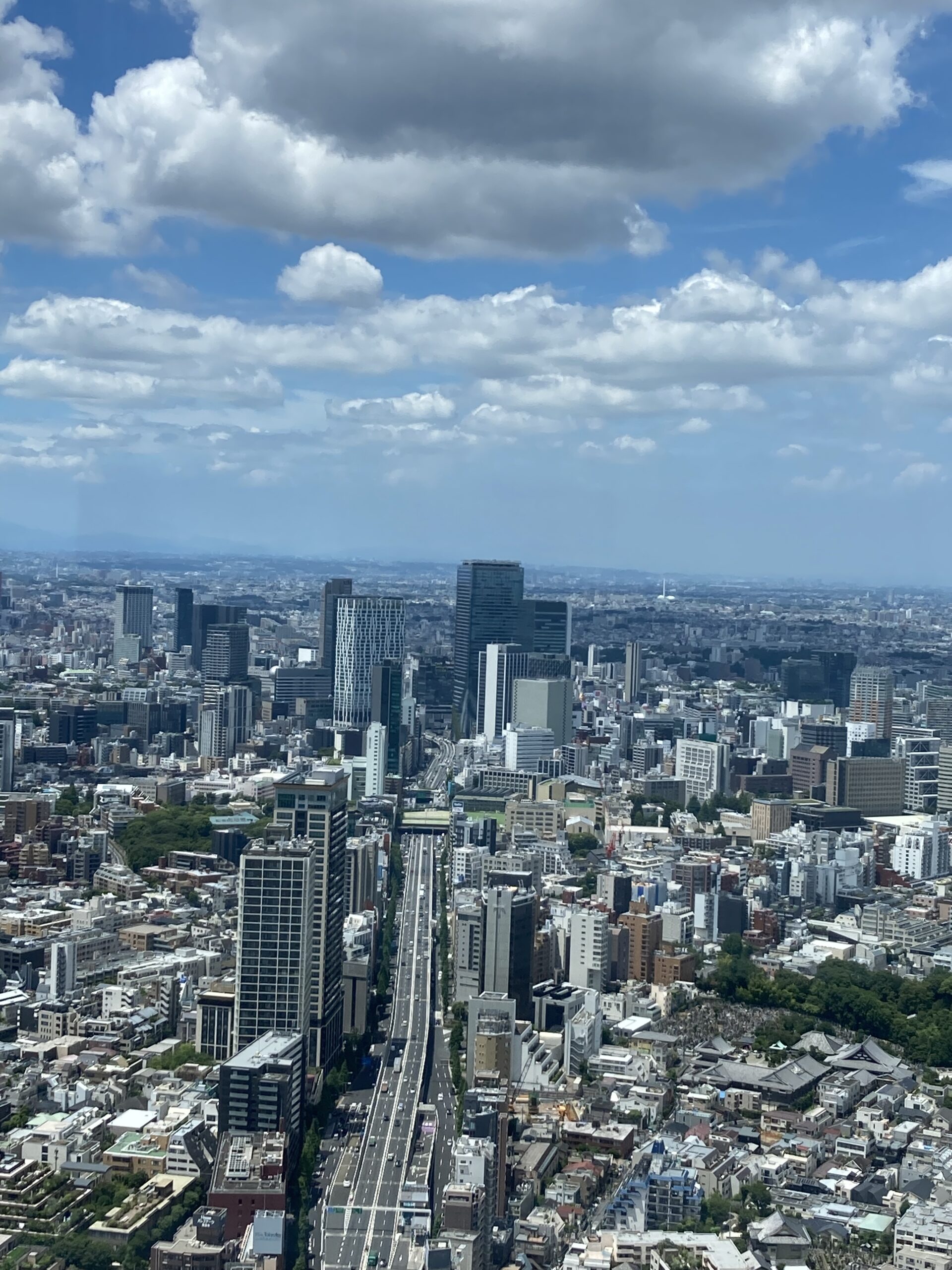 六本木ヒルズ展望台から見下ろした東京都心の景色。まっすぐに伸びる道路と高層ビルが立ち並び、青空に雲が浮かぶ開放的な風景。