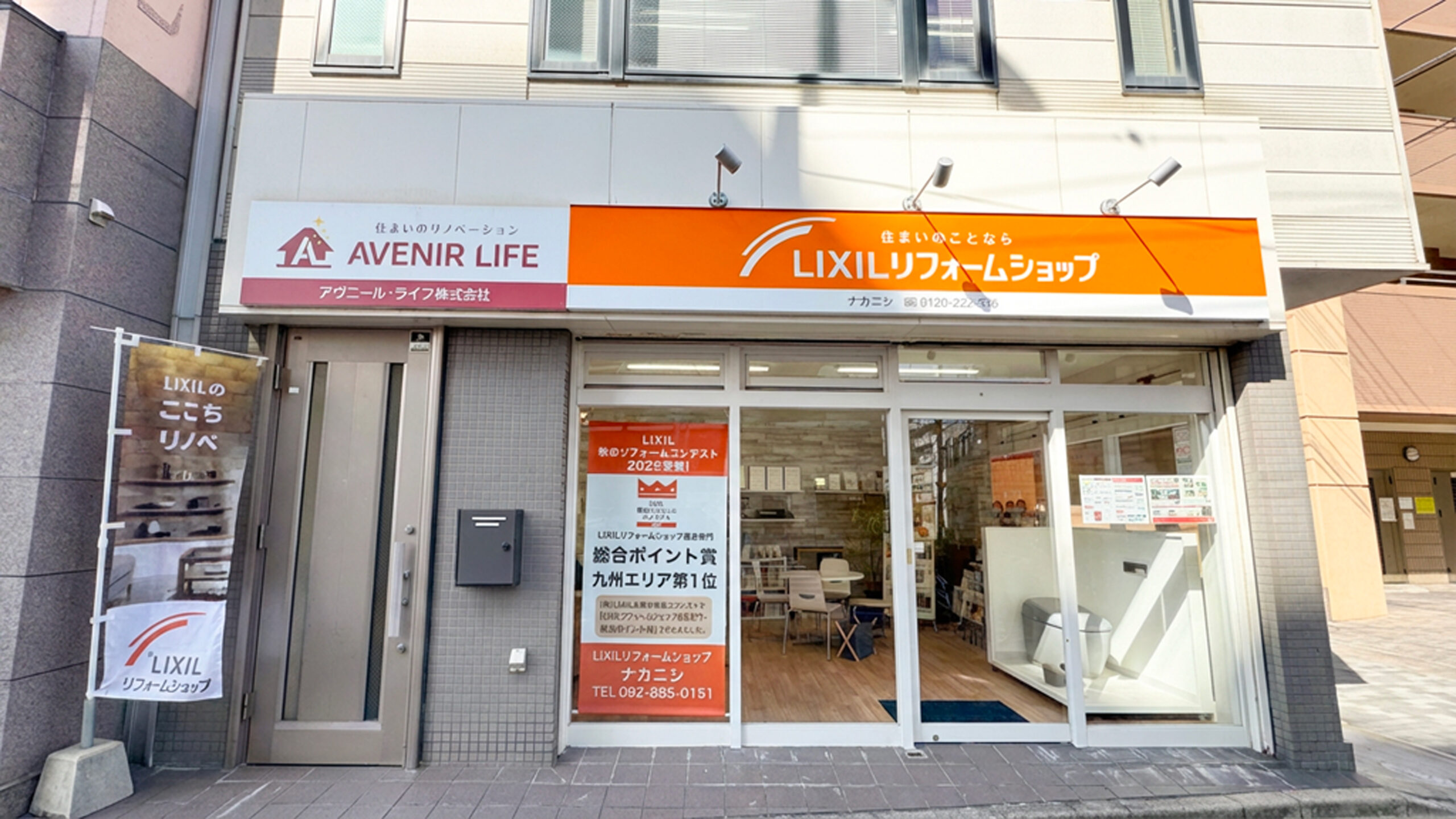 アヴニール・ライフ株式会社の店舗外観を正面から撮影した写真です。LIXILリフォームショップのオレンジ色の大きな看板が目を引き、ガラス面には「秋のリフォームコンテスト 九州エリア1位」の掲示も確認できます。